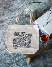 Load image into Gallery viewer, &quot;Creativity is contagious&quot; on a canvas tote bag in a swirl text effect

